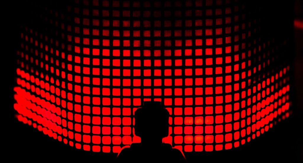 Une silhouette se détache devant un mur de carrés rouges.