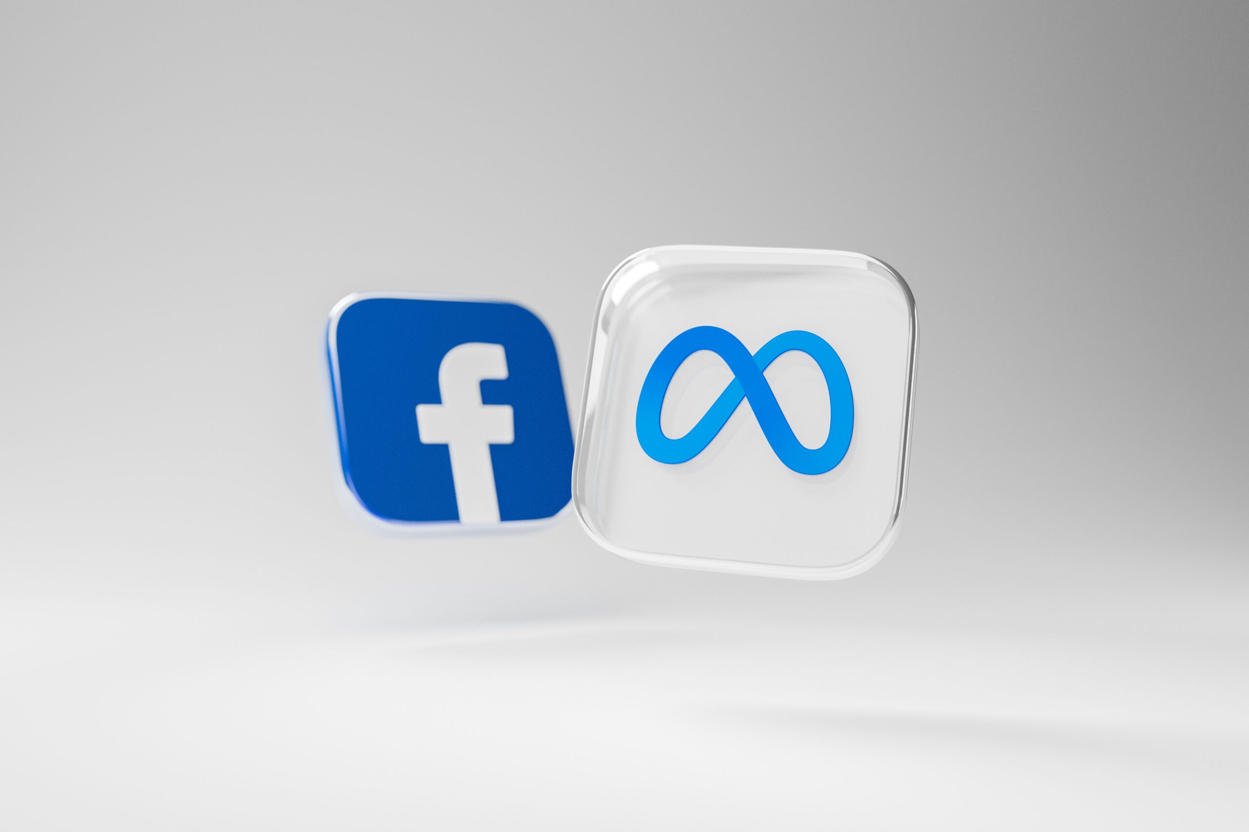 Les logos de Facebook et Meta dans des carrés en 3D sur un fond grisé dégradé