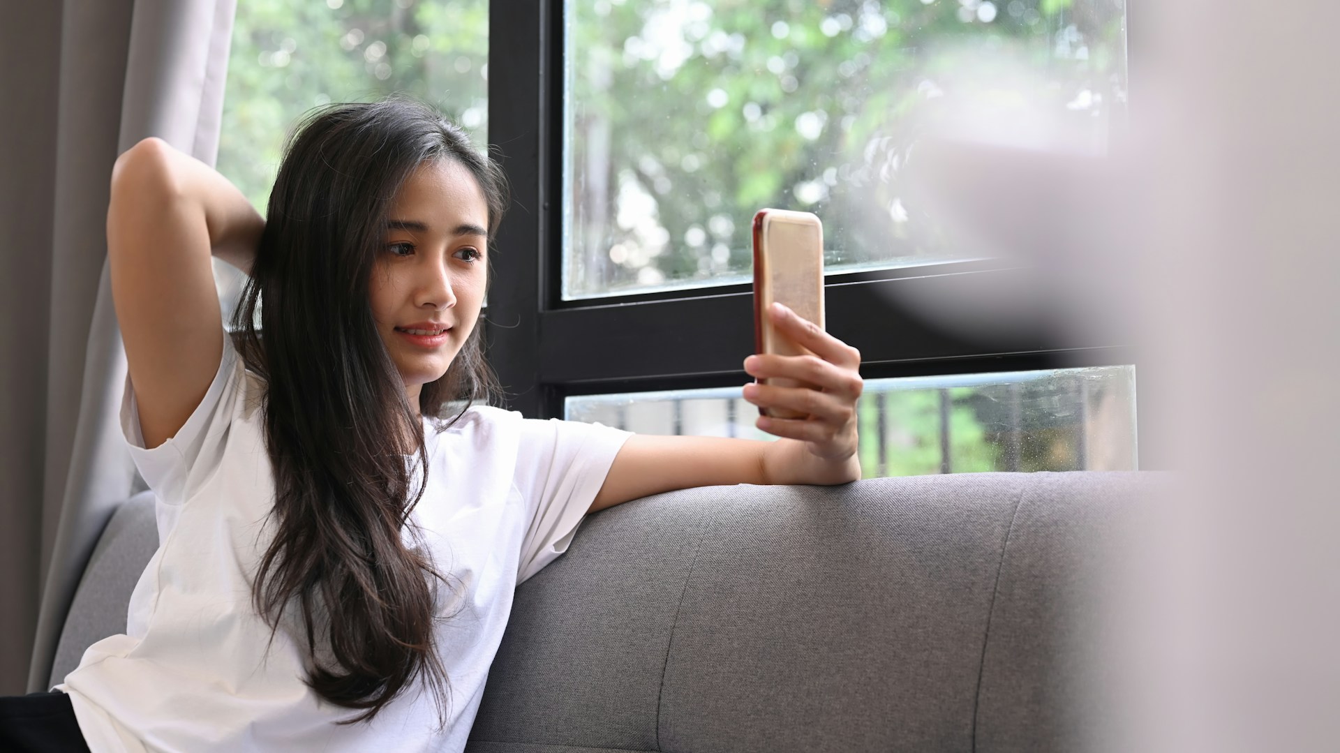 Une jeune fille assise sur un canapé se prend en selfie